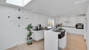 Une cuisine moderne dotée d’une verrière, de meubles blancs, d’un îlot central et d’une horloge murale originale.