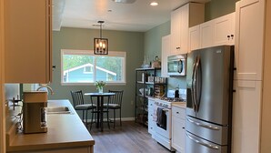 A modern kitchen with a dining area, featuring stainless steel appliances, wooden cabinets, and a window overlooking a house. - A charming country escape.  Near wineries, SLO, hiking, and SM Ranch & lake. (Santa Margarita)