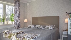 A bedroom with a large bed, two bedside lamps, a window with curtains, and a radiator.
