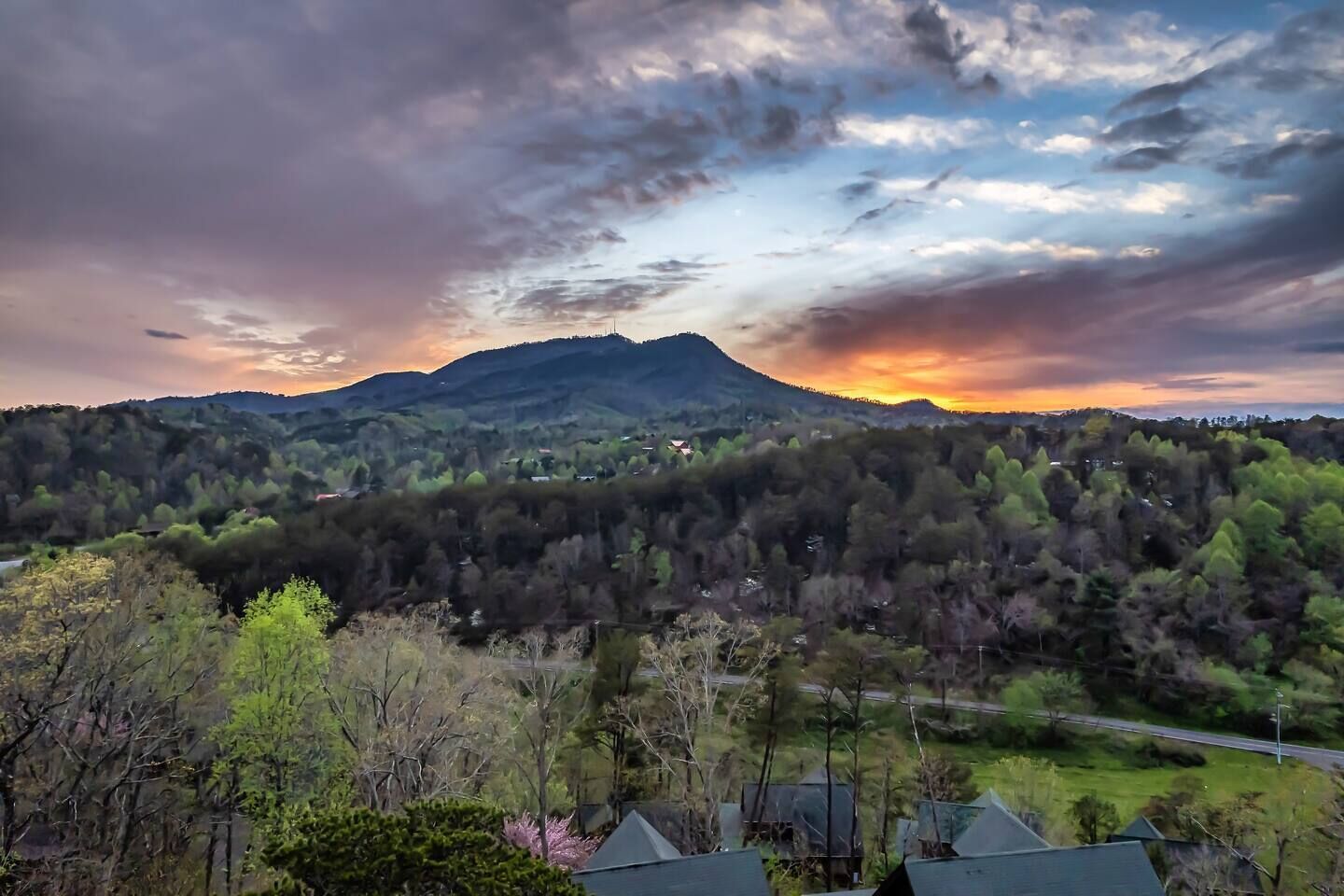 Un paisaje montañoso con atardecer, un bosque denso y edificios residenciales al frente.