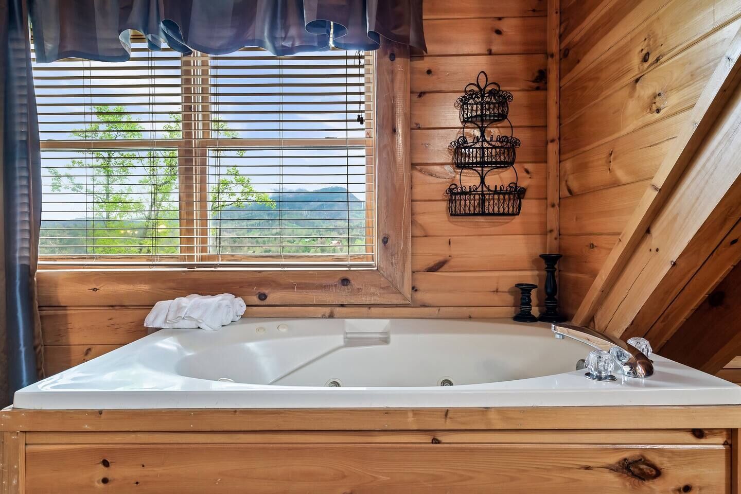 A wooden cabin interior with a large bathtub, a window with blinds, and a decorative metal wall piece.