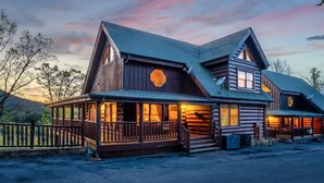 Eine Blockhütte mit Veranda und zahlreichen Fenstern vor einem Sonnenuntergangshimmel.