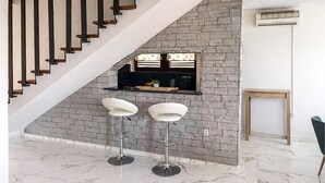 Une cuisine moderne avec un mur recouvert de pierres, un escalier en bois et deux tabourets de bar blancs.