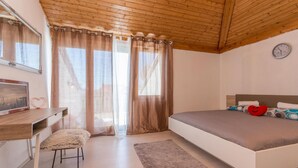 Une chambre avec un plafond en bois, un lit avec des oreillers, un bureau avec une chaise et une fenêtre avec des rideaux.