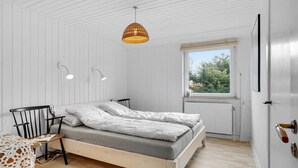 Ein Schlafzimmer mit Bett, Nachttischlampen, einem Fenster und Blick auf Grün.