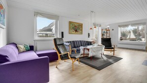 Ein geräumiges Wohnzimmer mit einem violetten Sofa, einem gestreiften Sessel und einem Holztisch.