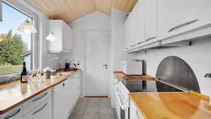 Eine moderne Küche mit weißen Schränken, Holz Arbeitsplatten, einem eingebauten Backofen und einem Fenster mit Blick auf Grünfläche.
