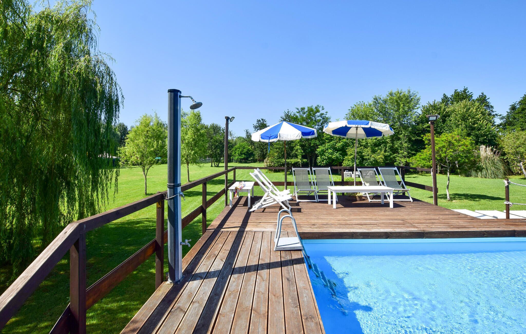 Une terrasse en bois avec une piscine, des chaises longues et des parasols.