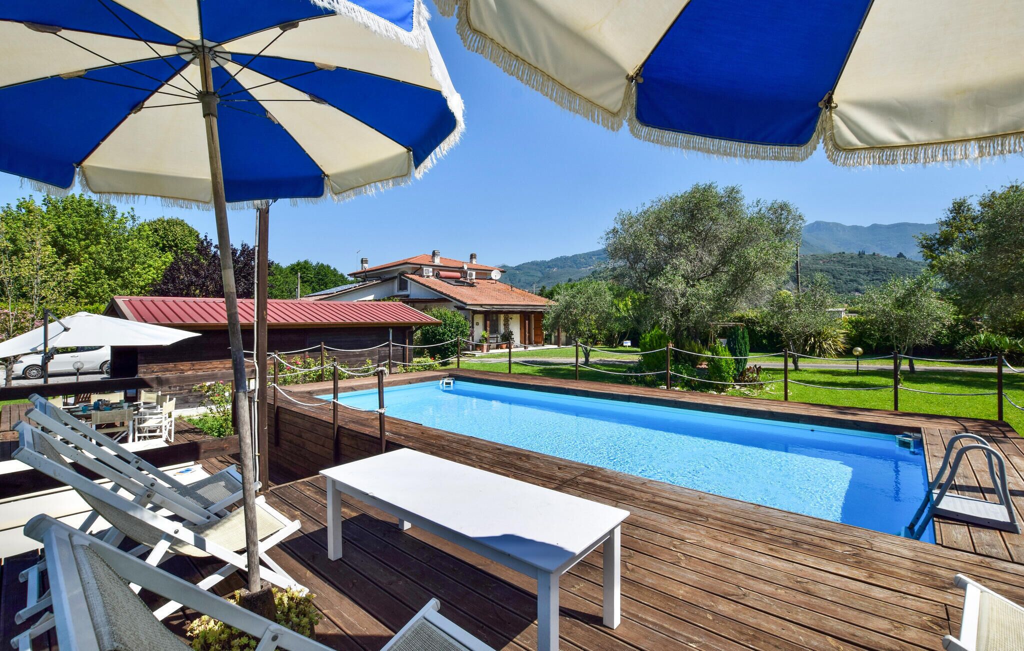 A wooden deck with a pool, lounge chairs, and umbrellas.