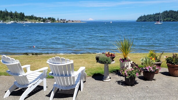 A waterfront view with two Adirondack chairs and potted plants on a gravel area. - Beachfront Home With Sweeping Views of Water and Mount Baker (Port Ludlow)