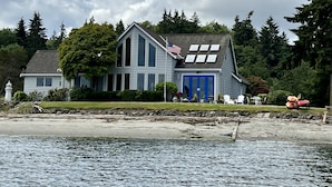 A two-story house with a blue front door and an American flag on the roof. - Beachfront Home With Sweeping Views of Water and Mount Baker (Port Ludlow)