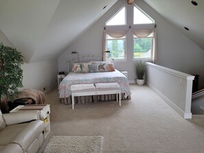 A bedroom with a sloped ceiling, a bed with floral bedding, a potted plant, a nightstand, and a window with curtains.