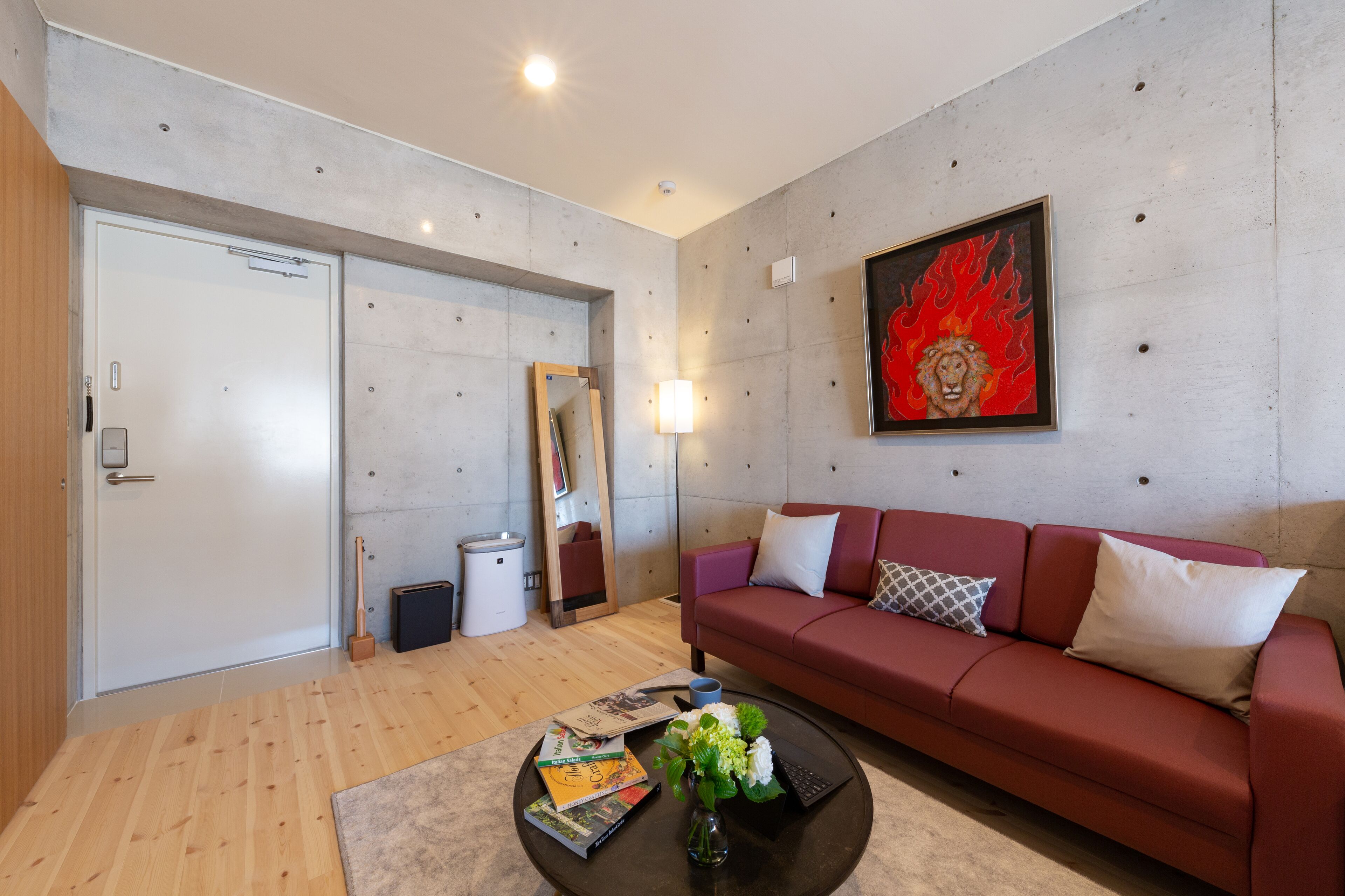 A modern living room with a red sofa, a coffee table with books and a vase, a painting on the wall, and a door with a mirror.