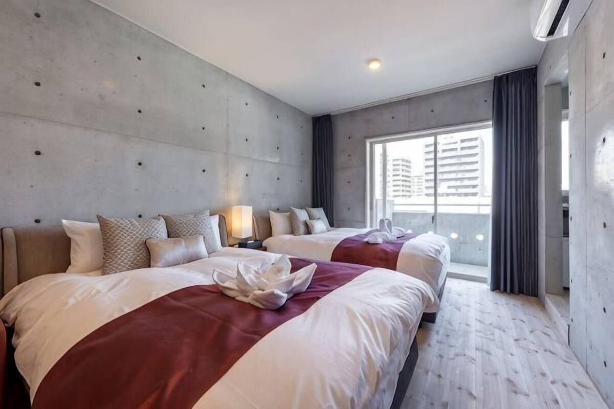 Habitación de hotel con dos camas, un ventanal grande y vistas a edificios.