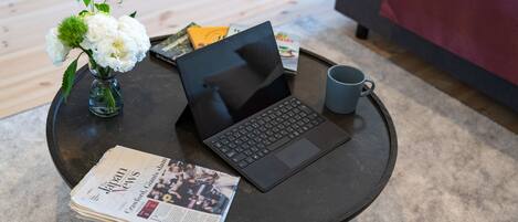A laptop on a round table with a newspaper, a mug, and a vase with flowers.