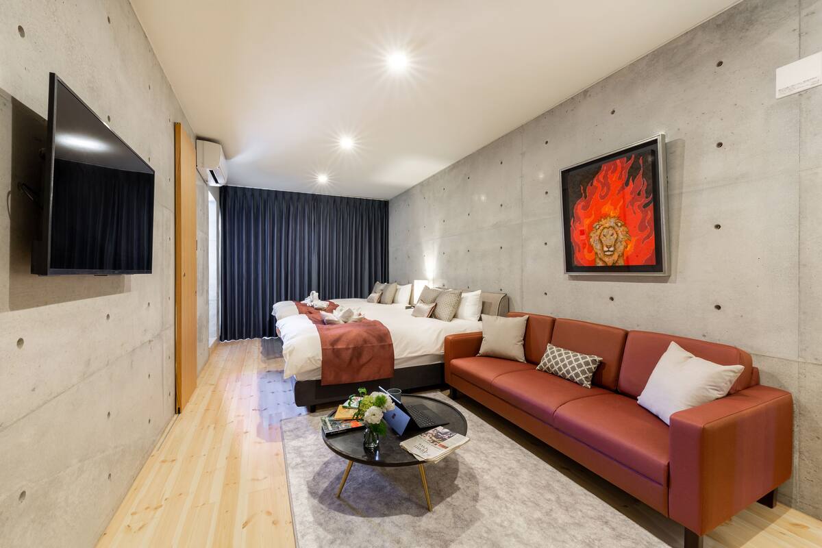Una habitación de hotel moderna con una cama grande, un sofá rojo, un televisor de pantalla plana y un cuadro de un león en la pared.