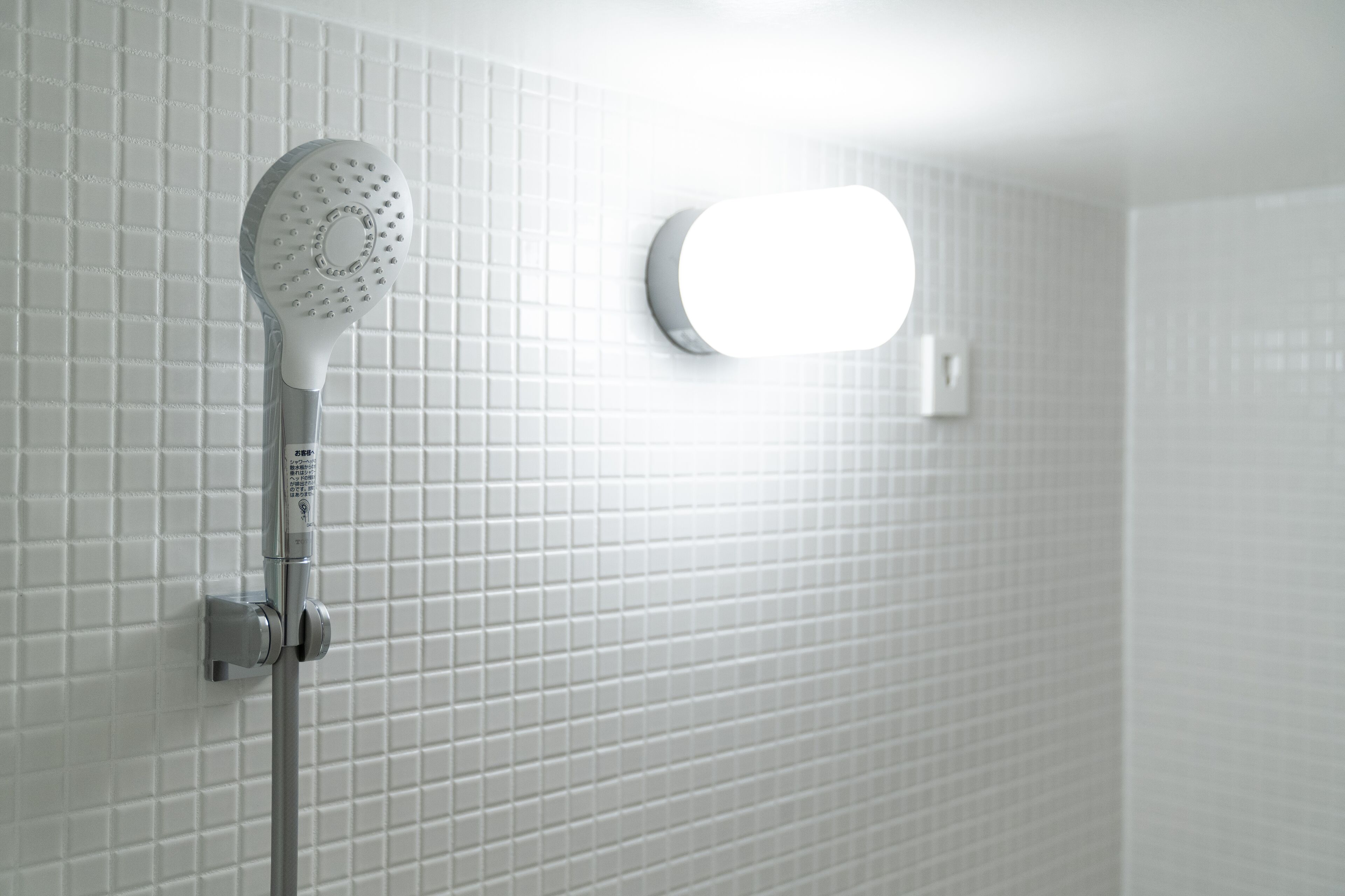 A shower with a handheld showerhead mounted on a wall with white tiles.