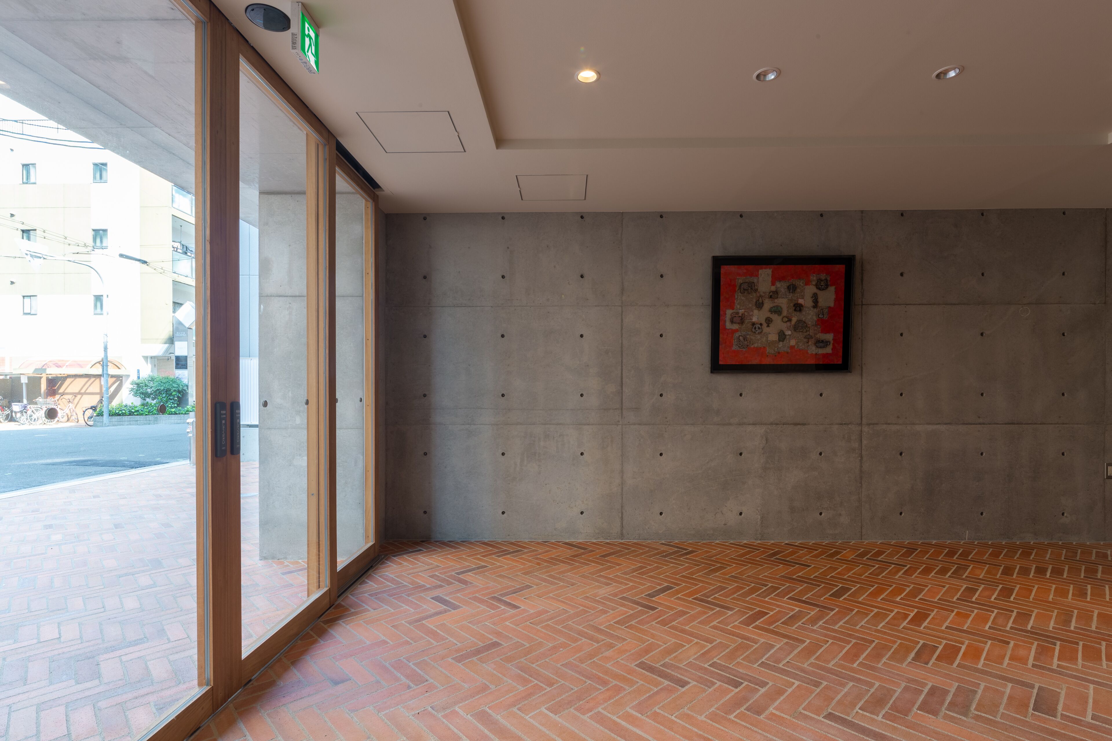 Eine Hotelhalle mit einem Fischgrätparkettboden, großen Fenstern und einer Betonwand mit einem gerahmten Kunstwerk.
