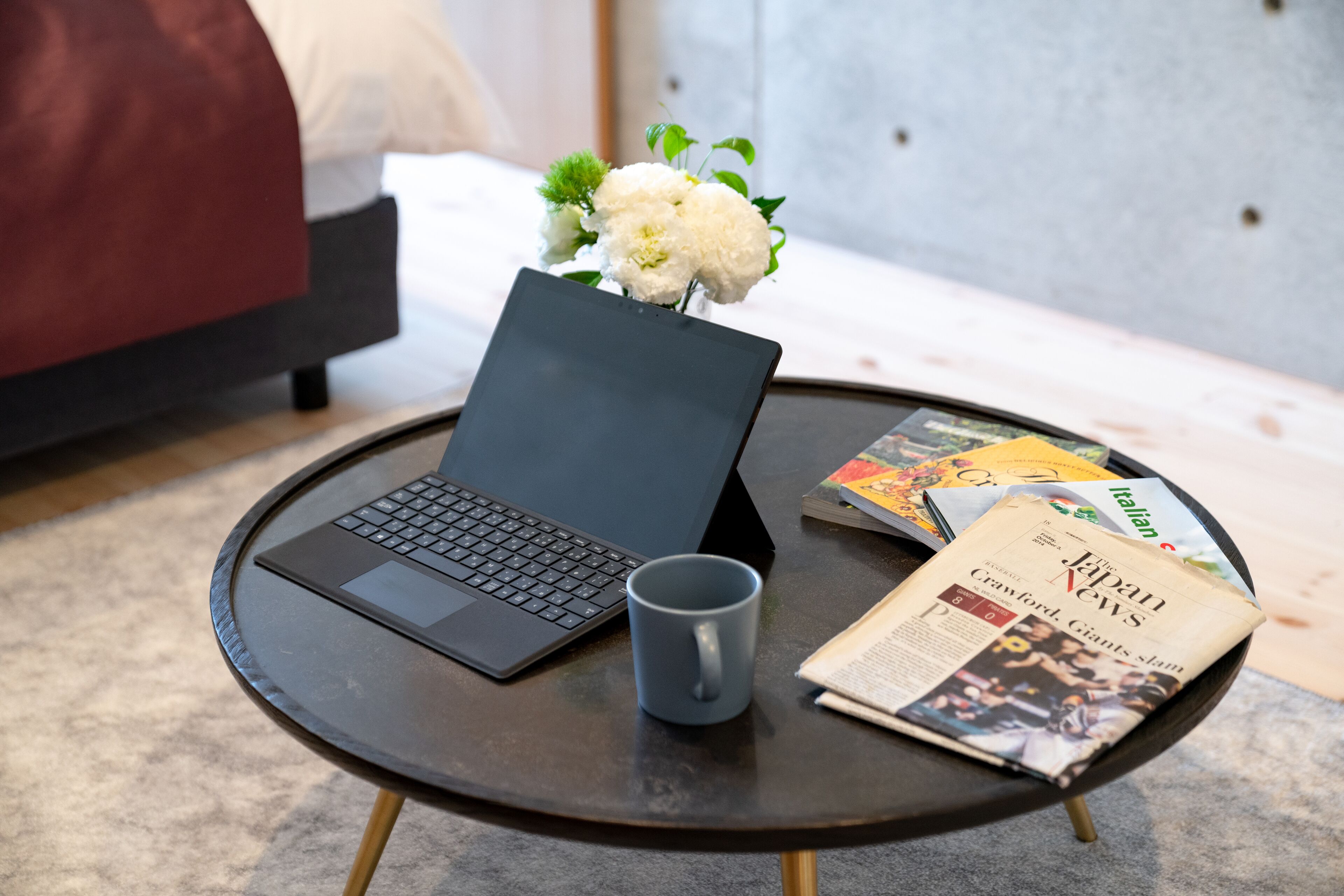 A laptop on a round table with a mug and a newspaper.