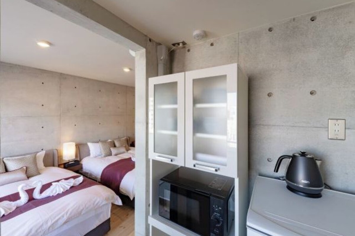 Une chambre d’hôtel avec deux lits, un four à micro-ondes, une bouilloire et un meuble avec des portes en verre dépoli.