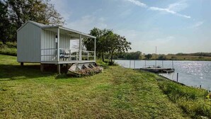 A small, single-story cabin with a porch and a dock extending into a lake. - Corn Crib Cottage (Crab Orchard)