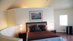 A bedroom with a large bed, two bedside tables with lamps, a framed picture on the wall, and a window with blinds. - Corn Crib Cottage (Crab Orchard)