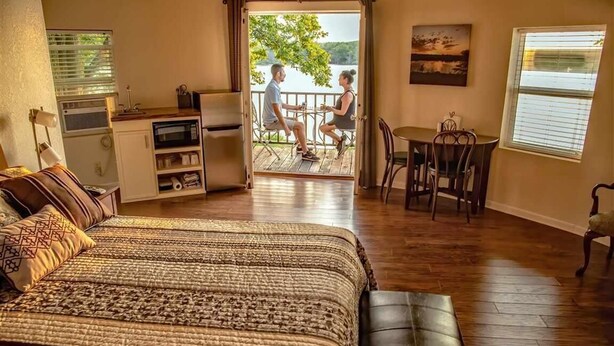 A cozy room with a bed, a dining table, and a balcony with a view of a lake. - Corn Crib Cottage (Crab Orchard)