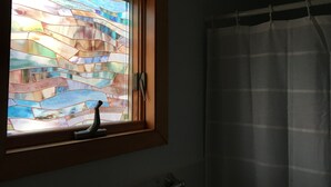 A bathroom with a stained glass window, a shower curtain, and a towel rack.