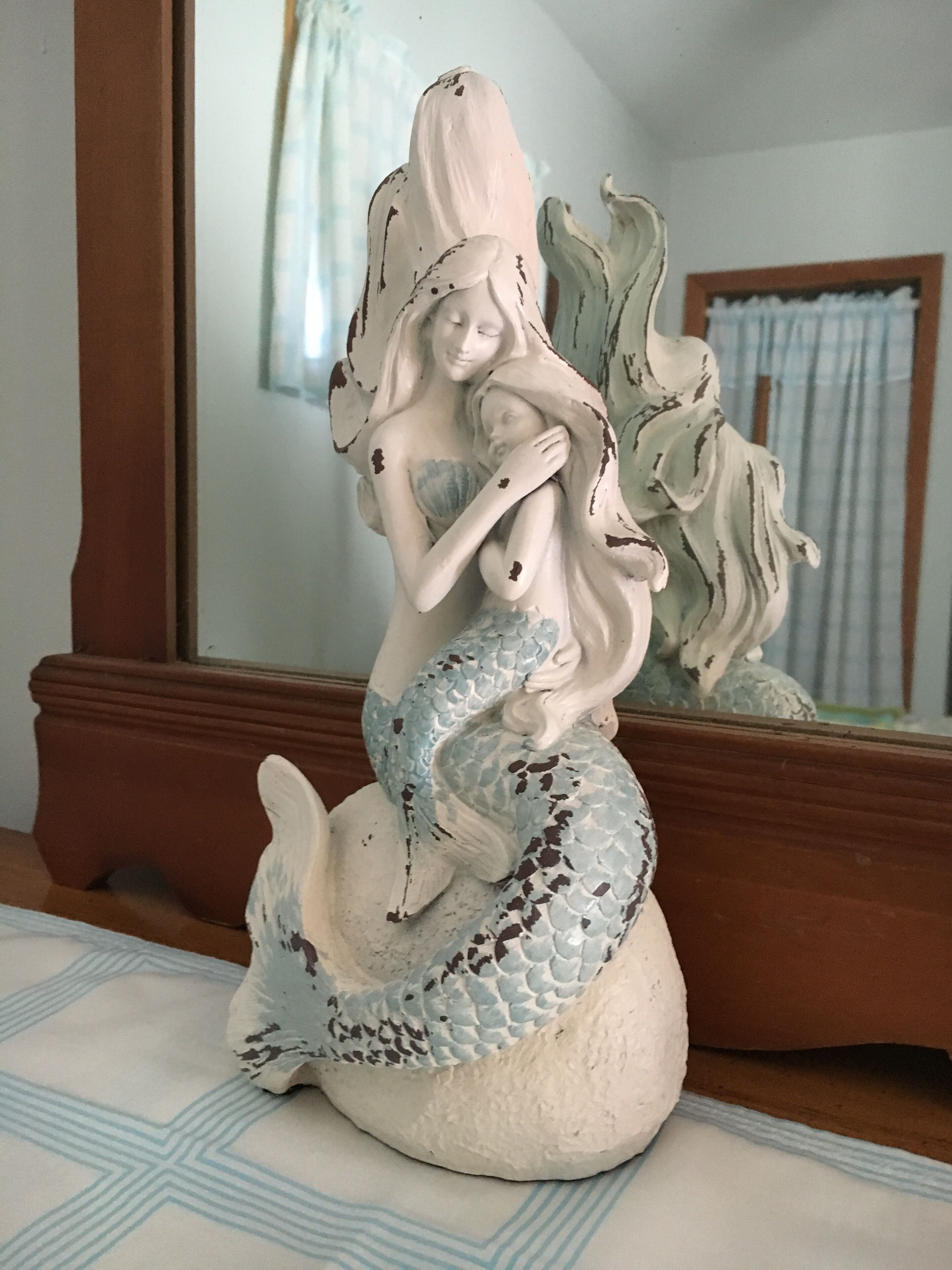 Eine Meerjungfrau-Statue mit einem Kind auf einer gemusterten Tischdecke.