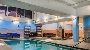 An indoor swimming pool with lounge areas, towels on shelves, and a view of the outside.