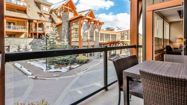 A balcony with wicker furniture, a view of a ski resort, and a building with wooden architecture.