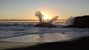 A beach with waves crashing against rocks during sunset.