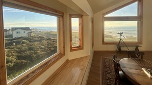 A room with large windows offering ocean views, a dining area with a table and chairs, and a tripod with a camera.