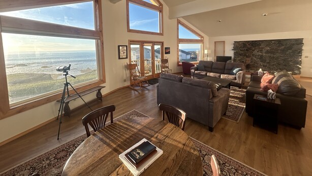A spacious living room with large windows, a stone fireplace, and a dining area with a table and chairs.