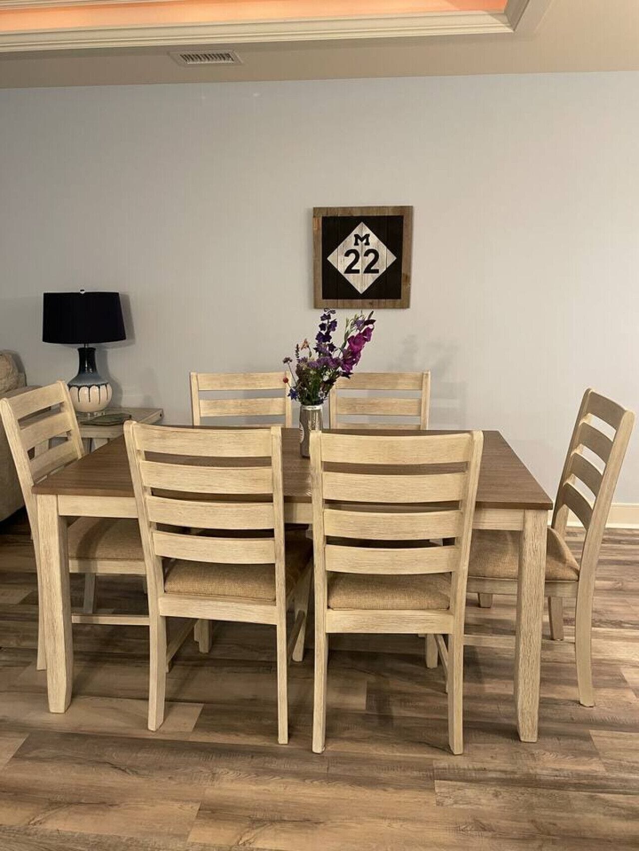 A dining area with a wooden table and chairs, a vase with flowers, and a wall-mounted sign with the number 22.