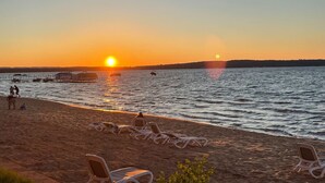 A beach with sun loungers and people walking along the shore. - Beachy Condo with Pool & Hot Tub (Traverse City)