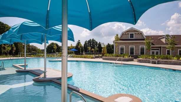 A swimming pool with blue umbrellas, a poolside area, and a building in the background. - Bright & Airy House. Child friendly, EV charging, Pool, sauna, gym, kayak+ (Ocean View)