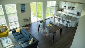 A modern open-plan living and dining area with a sofa, dining table, and chairs. - Bright & Airy House. Child friendly, EV charging, Pool, sauna, gym, kayak+ (Ocean View)