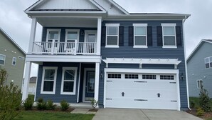 A two-story house with a front porch, a garage, and a small front yard. - Bright & Airy House. Child friendly, EV charging, Pool, sauna, gym, kayak+ (Ocean View)
