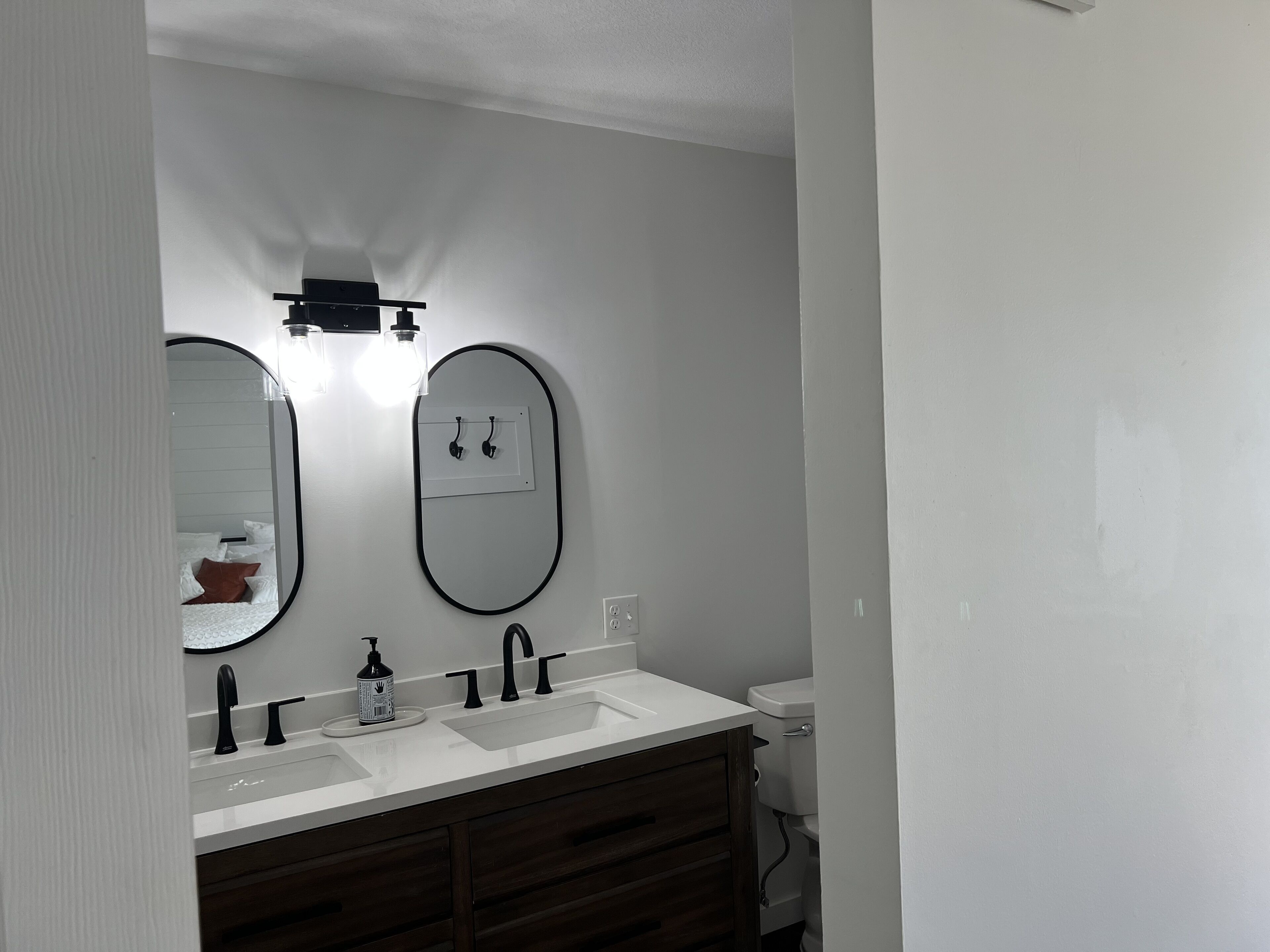 A bathroom with a double sink, two mirrors, a light fixture above the mirrors, and a toilet visible to the right.
