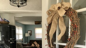 A kitchen with a black refrigerator, a dining area with a patterned sofa, and a decorative wreath on a door. - Charming Riverside Cottage on 5 Acres- Perfect for Couples & Nature Lovers (Amherst)