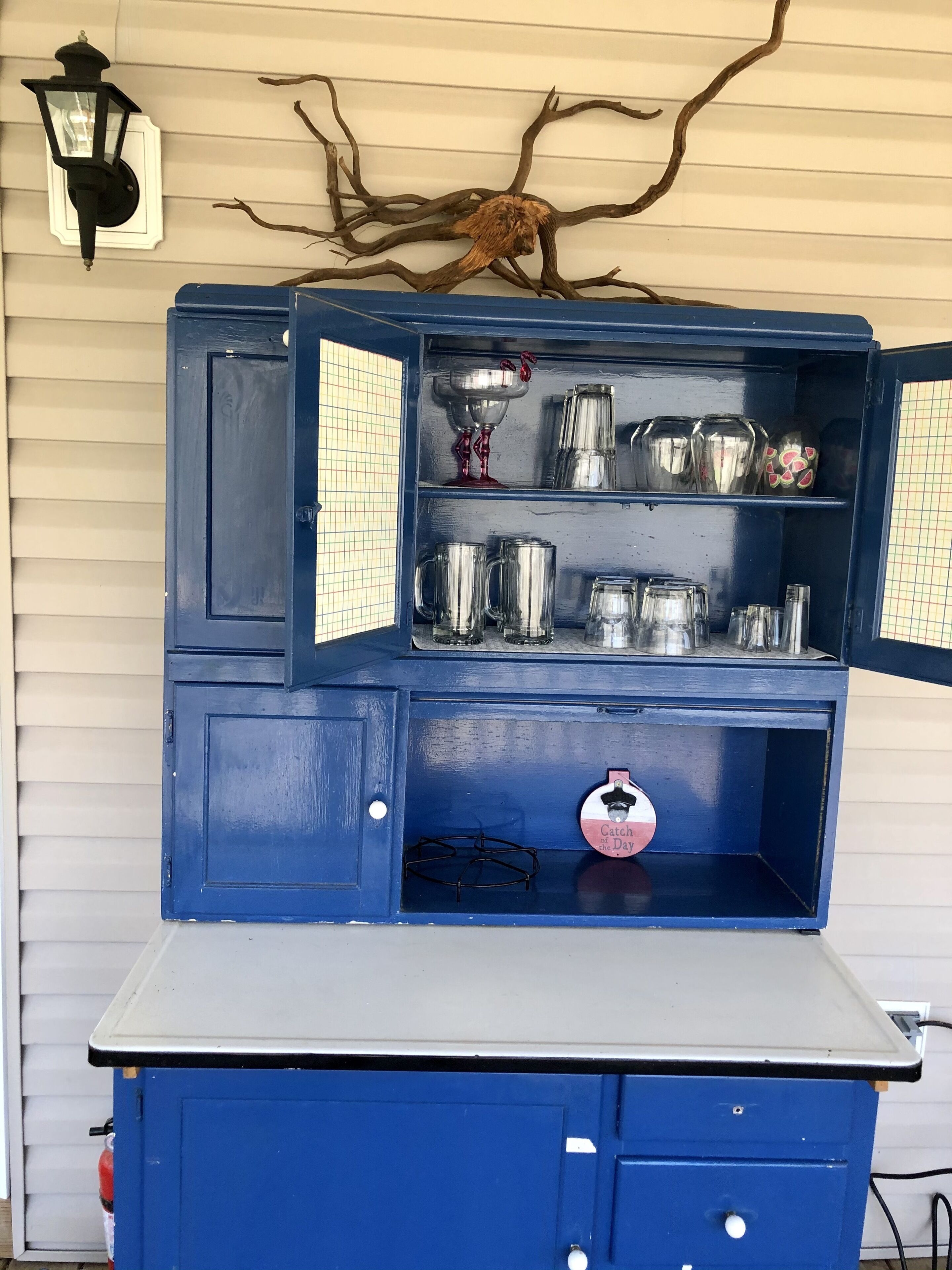 A blue cabinet with open shelves displaying various kitchenware and a decorative piece labeled "Catch of the Day."