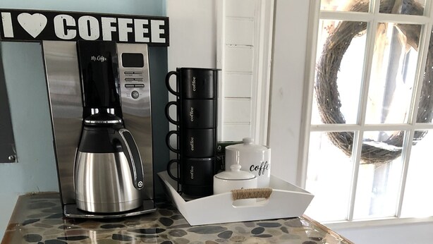 A kitchen counter with a coffee maker, a coffee pot, and a coffee mug. - Charming Riverside Cottage on 5 Acres- Perfect for Couples & Nature Lovers (Amherst)