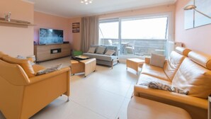 Un salon moderne comprenant un canapé, un téléviseur et un balcon aménagé avec du mobilier d’extérieur.