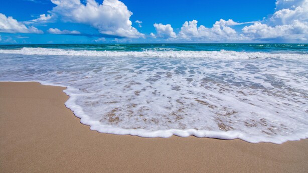 Ein Strand mit klarem, blauem Wasser und weißen Schaumwellen.