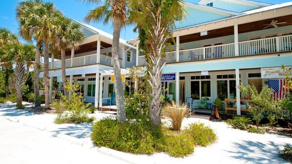 Un hotel frente a la playa con una estructura de dos pisos, mobiliario exterior y palmeras.