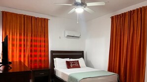 Quarto com cama, mesa de cabeceira, televisão e ventoinha no teto.