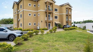 Um edifício residencial de vários andares com telhado plano, várias varandas e um gramado bem cuidado.