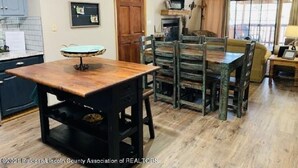 Uma zona de refeições rústica com uma mesa de madeira e bancos, uma cozinha com revestimento de azulejos e uma janela grande com vista.
