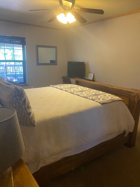 Een slaapkamer met een bed, een plafondventilator, een televisie en een raam met jaloezieën.